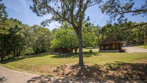 A rustic cabin with a porch, surrounded by a grassy area and trees.