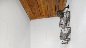 Une douche aux murs recouverts de carreaux blancs, un plafond en bois et un sol dont le motif rappelle des galets.