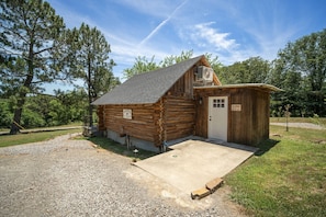 A rustic log cabin with a small attached shed, a gravel driveway, and a clear sky. - The Velvet Rooster – Cozy Cabin Stay with Pasture Views & Modern Comforts (Rudy)