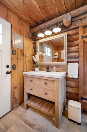 A wooden cabin bathroom with a white sink, a mirror, and a small white toilet. - The Velvet Rooster – Cozy Cabin Stay with Pasture Views & Modern Comforts (Rudy)