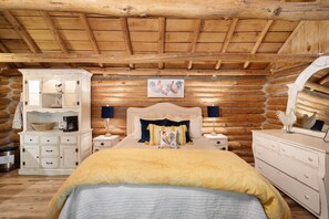 A rustic log cabin bedroom with a bed, bedside tables, a dresser, and a mirror. - The Velvet Rooster – Cozy Cabin Stay with Pasture Views & Modern Comforts (Rudy)
