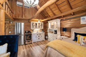 A log cabin interior with a kitchen, dining area, and a bedroom.