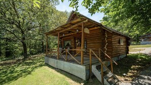 Eine rustikale Holzhütte mit Veranda und kleiner Terrasse, umgeben von Bäumen.