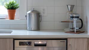 Cocina moderna con armarios de madera, lavavajillas de acero inoxidable, cafetera y una planta en el alféizar.