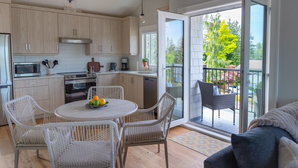 Una cocina moderna con gabinetes blancos, un comedor con sillas de mimbre y un vidrio corredizo que da a un patio exterior.