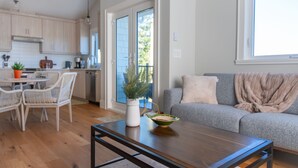 Una sala de estar moderna con una mesa de centro de madera, un sofá gris y un comedor con sillas blancas y una mesa pequeña.