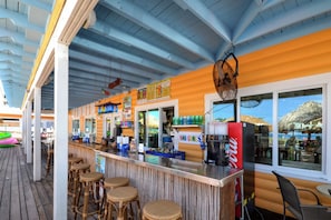 Uma área de bar com balcão, banquetes e vista para o mar através de grandes janelas.