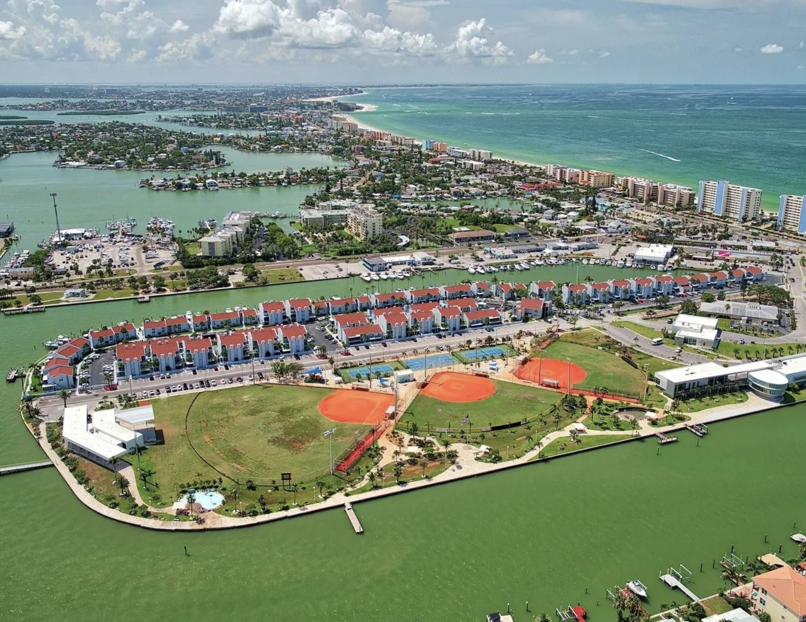 Vista aérea de un complejo turístico costero con varios edificios hoteleros, un puerto deportivo e instalaciones deportivas.