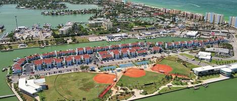 Vista aérea de un complejo turístico costero con varios edificios hoteleros, un puerto deportivo e instalaciones deportivas.