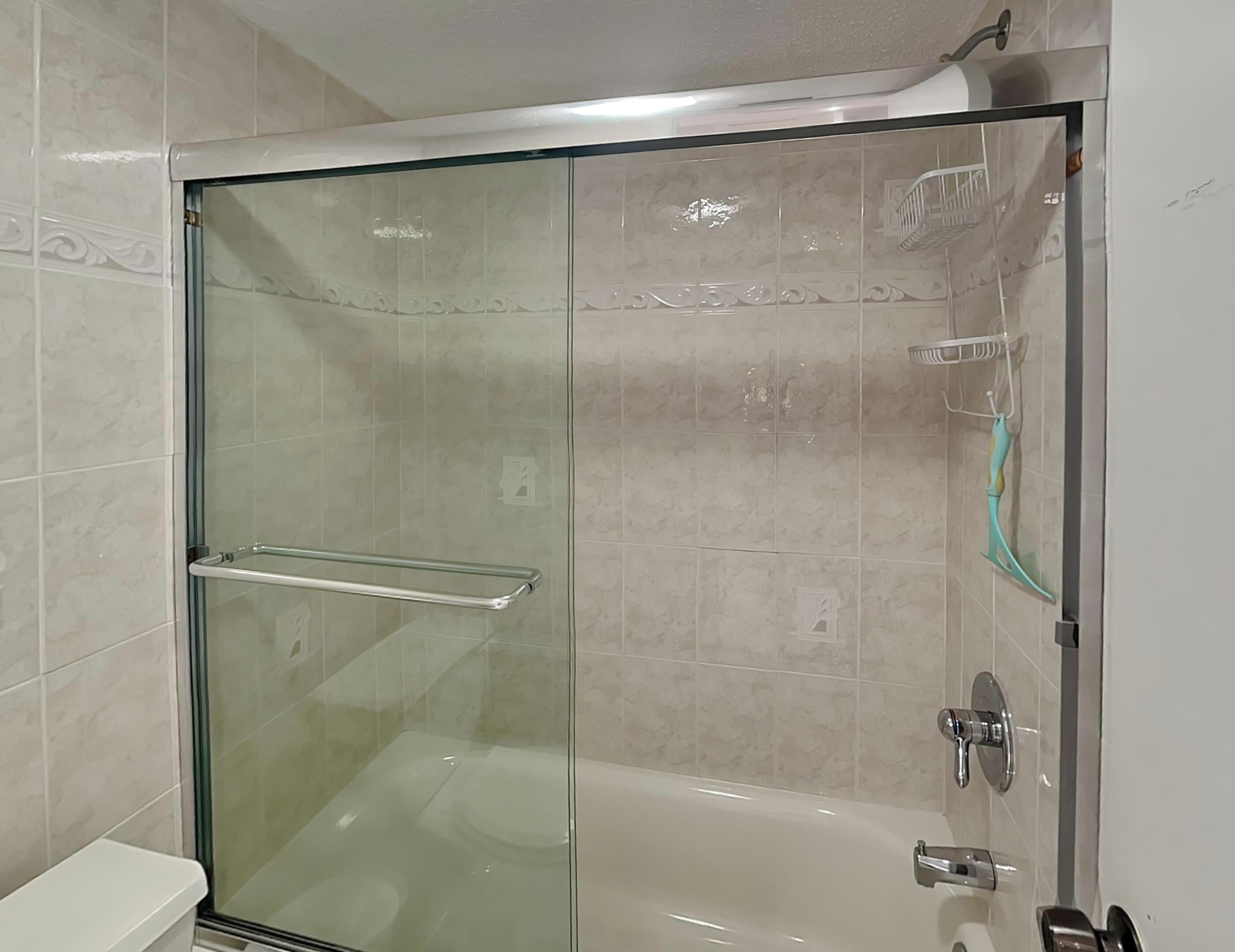 A glass-enclosed shower with a glass door, a glass shower curtain, and a handheld showerhead.