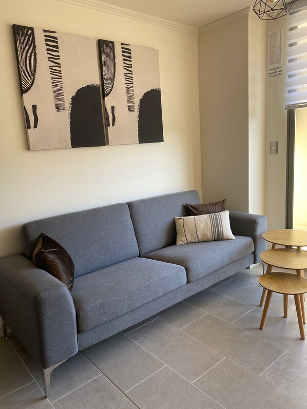 Un salon moderne avec un canapé gris, deux petites tables d’appoint rondes en bois et des œuvres d’art abstraites accrochées au mur.