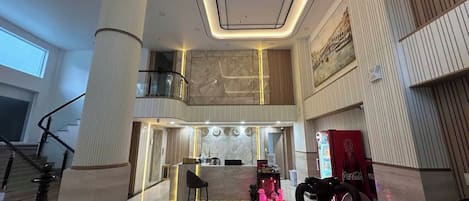Un vestíbulo de hotel con una mesa de recepción, una máquina expendedora de Coca-Cola y una escalera.