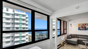 A modern hotel room with a large window, a sofa, and a bed.