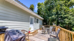 A wooden deck with outdoor furniture, a barbecue grill, and a small porch area with steps leading to a door.