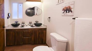 A bathroom with a wooden vanity, a white toilet, and a window.
