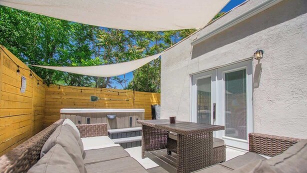 An outdoor patio with a wooden deck, wicker furniture, and a hot tub.