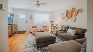 A living room with a sofa, ottoman, and chairs, a ceiling fan, and a wall with decorative plates.