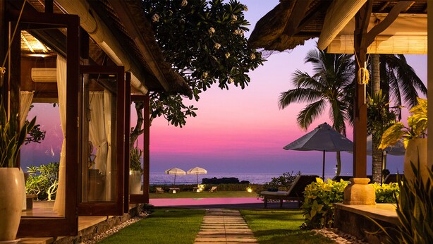 A pathway leading to a pool area with lounge chairs and umbrellas, overlooking a body of water at sunset. - Villa Tanju by Elite Havens (Cemagi)