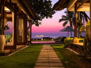 A pathway leading to a pool area with lounge chairs and umbrellas, overlooking a body of water at sunset. - Villa Tanju by Elite Havens (Cemagi)