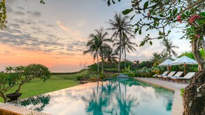 A serene pool area with lounge chairs, palm trees, and a view of the sunset. - Villa Tanju by Elite Havens (Cemagi)
