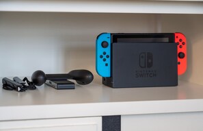 En Nintendo Switch-konsol med två Joy-Con-kontroller, en laddningsstation och en USB-kabel, placerad på en vit yta.
