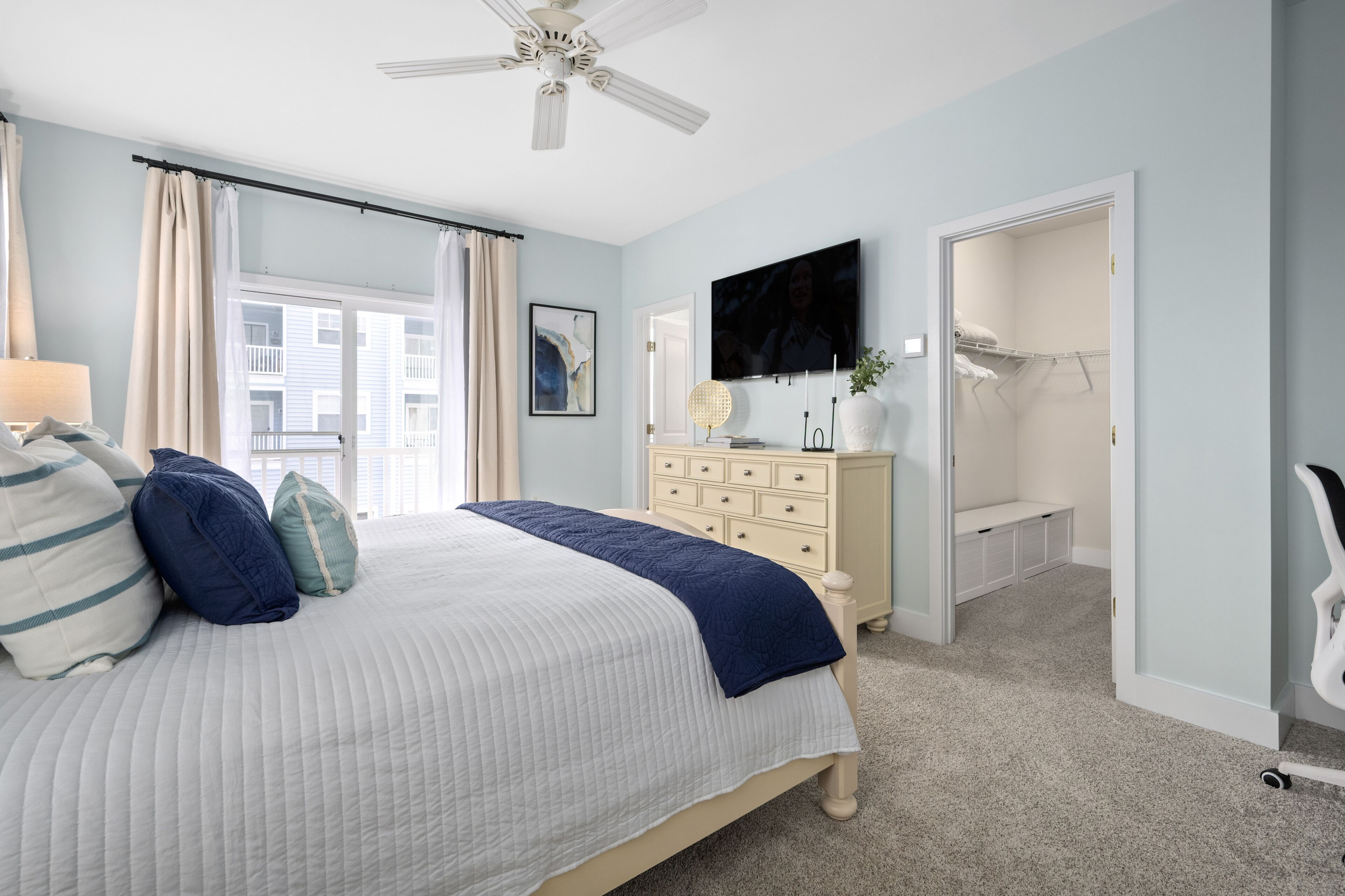 A bedroom with a bed, a dresser, a television, and a walk-in closet.