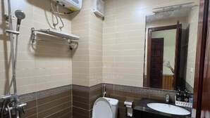 A bathroom with a toilet, sink, and shower. There is a towel rack and a mirror. - Doi Che Hotel - by Bay Luxury (Ho Chi Minh City)