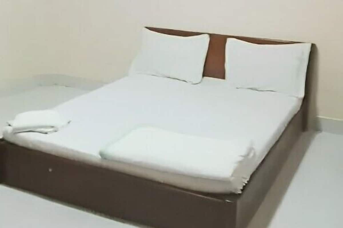 A neatly made bed with white linens and a wooden headboard in a simple room with a single wall-mounted painting.