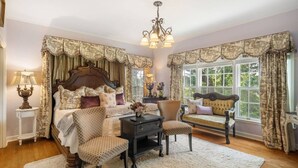 A bedroom with a large bed, two chairs, a small table, and a window with curtains. - Beland Mansion Getaway – Spacious Colonial with Game Room & Lounge (Fort Smith)