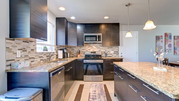 A modern kitchen with dark cabinetry, a granite countertop, stainless steel appliances, and pendant lighting.