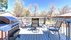 A deck with a grill, chairs, and a view of trees.
