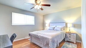 A bedroom with a bed, bedside tables, a ceiling fan, a window, and a desk.