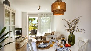 Ein heller, offener Wohn- und Essbereich mit großem Fenster, einem runden Esstisch, der für ein Frühstück gedeckt ist, und einer gemütlichen Sitzecke mit Sofa und Sesseln.