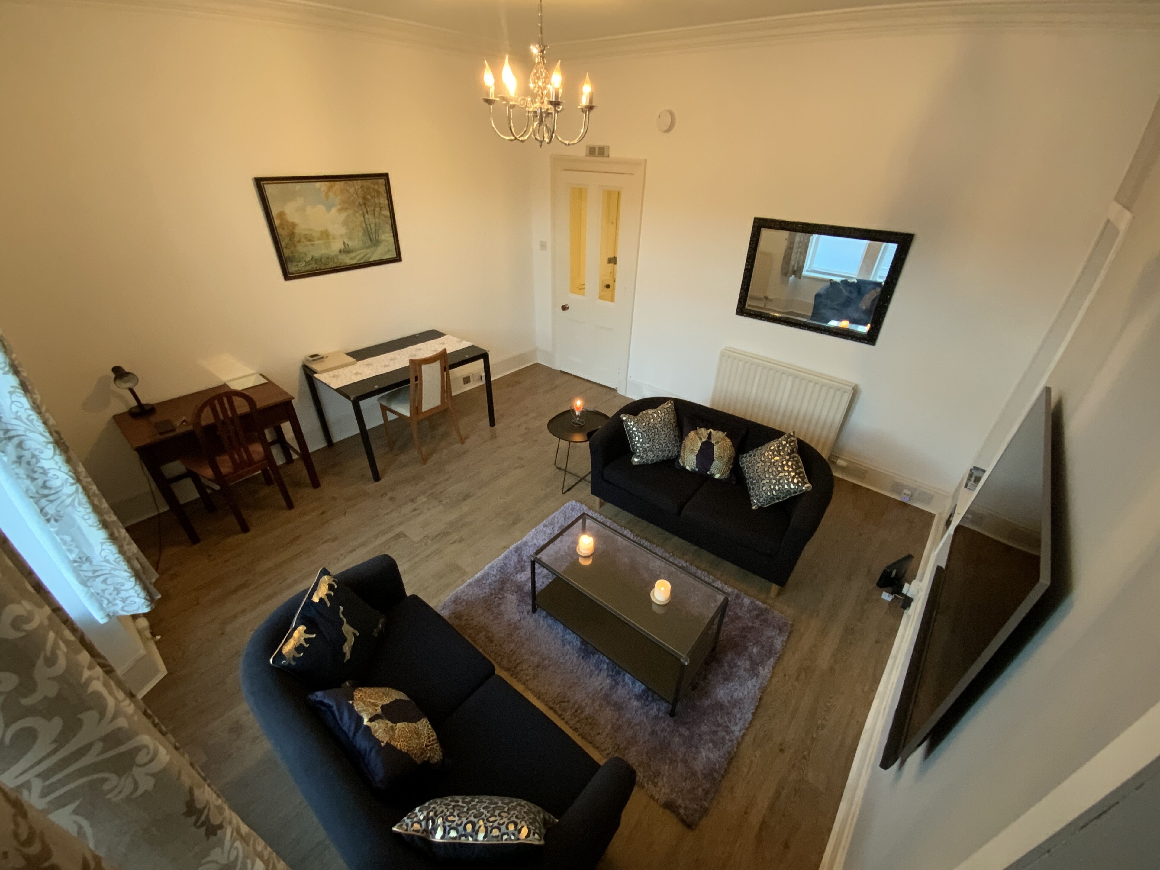 Un salon comprenant un canapé, une table basse, une table à manger avec des chaises, un lustre, un tableau et un miroir.