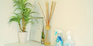 Una planta en maceta, difusor de cañas, certificado enmarcado y productos de limpieza sobre una mesa.