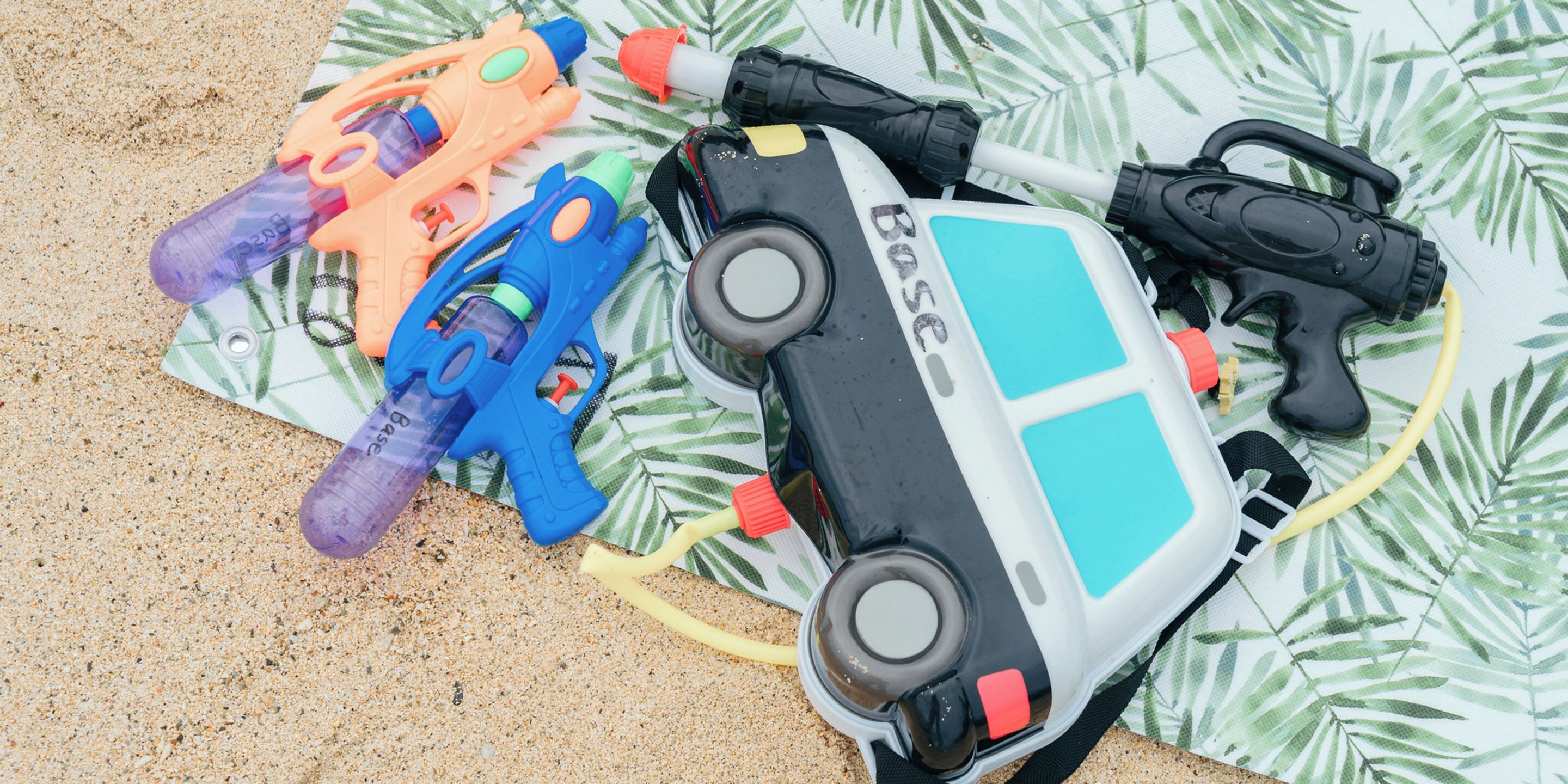 A beach scene with a surfboard, a toy gun, and a toy car on a patterned fabric.