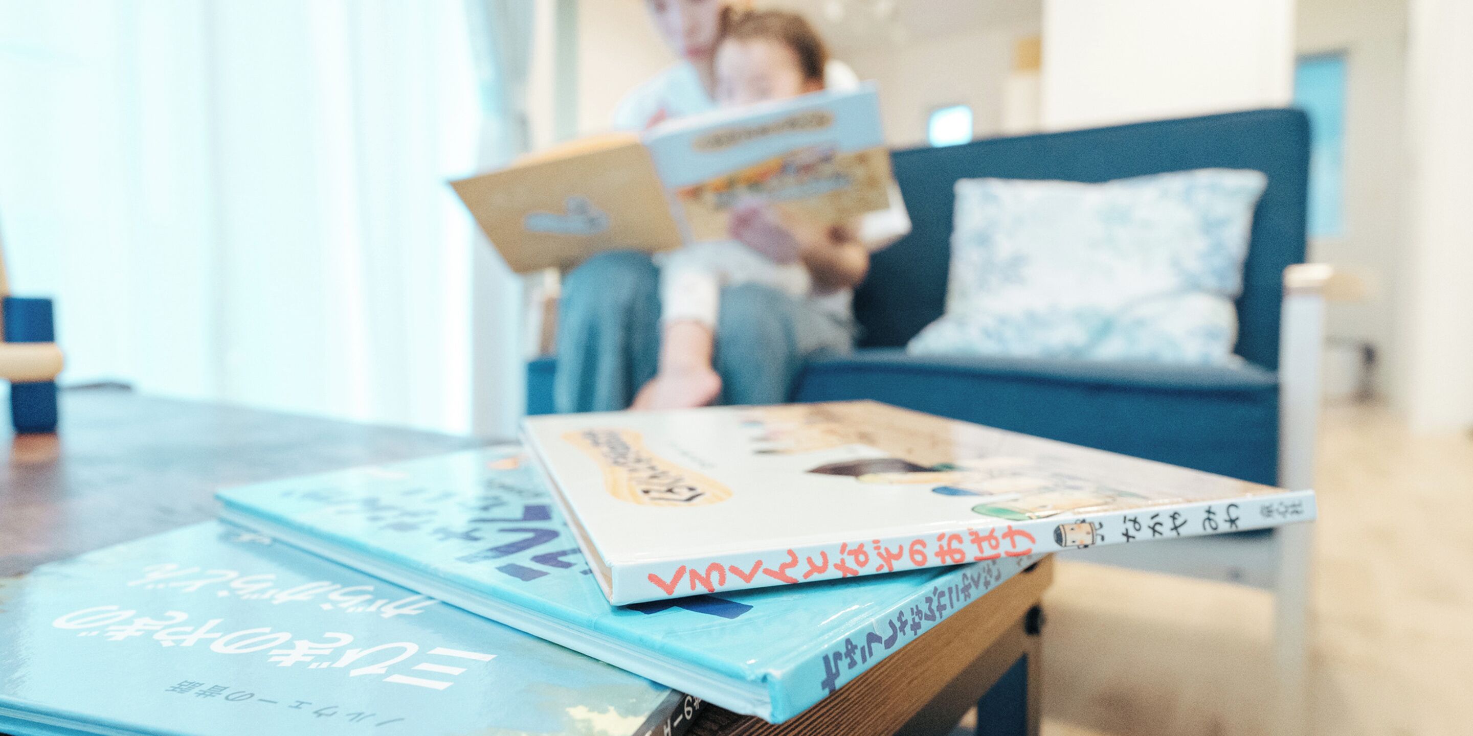 A room with a blue sofa, a coffee table with books, and a person reading a book.