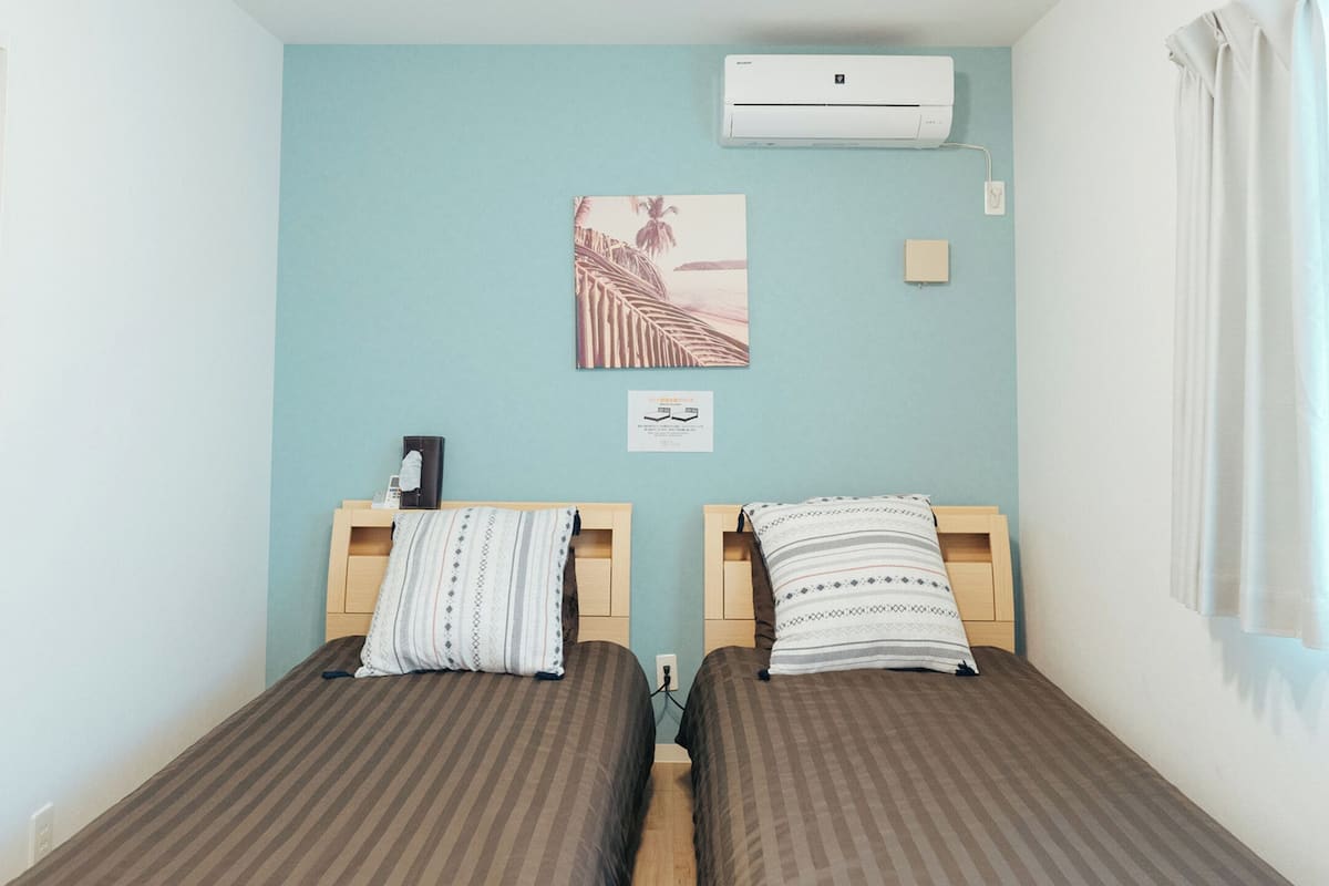 A twin room with two beds, a wall-mounted air conditioner, a framed picture, and a small bedside table.