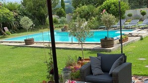 Un patio al aire libre con mobiliario de mimbre, una sombrilla roja y una piscina al fondo.