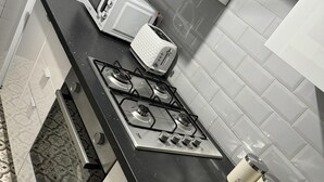 A kitchen with a gas stove, a microwave, and three labeled containers for tea, coffee, and sugar.