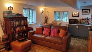 A cozy living room with a brown leather sofa, a wooden bookshelf, and a kitchen area with a microwave and cabinets.