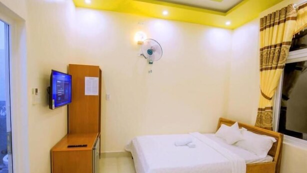 A hotel room with a bed, a desk, a television, and a wall-mounted fan. - Thien Thuan Hotel - by Bay Luxury (Ho Chi Minh City)