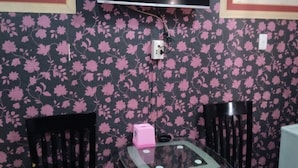 A small room with a TV mounted on the wall, two black chairs, a glass table, and a wicker basket. - Thien Thuan Hotel - by Bay Luxury (Ho Chi Minh City)