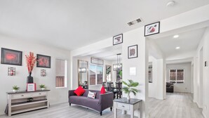 Una sala de estar moderna con un sofá gris, una mesita de noche blanca y una alfombra negra. Hay cuadros enmarcados en las paredes y un espejo sobre el sofá.