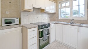 A kitchen with white cabinets, a microwave, a stove, and a window. - Marine Lodge -  a bungalow that sleeps 4 guests  in 2 bedrooms (Bognor Regis)