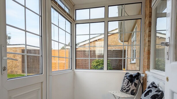 A corner room with a bay window, a white door, and a small white table with cushions. - Marine Lodge -  a bungalow that sleeps 4 guests  in 2 bedrooms (Bognor Regis)
