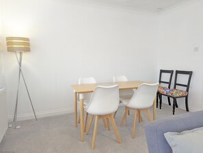 Un coin repas avec une table en bois et des chaises blanches, un lampadaire et un canapé agrémenté d’un coussin.