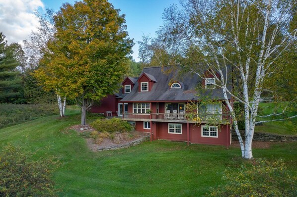 A two-story house with a balcony, surrounded by trees and a well-maintained lawn. - Mountain View Estate with Game Room & Valley Views (Quechee)