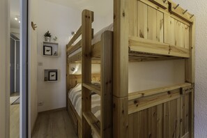 A room with a bunk bed, a small shelf with framed pictures, and a door leading to another room. - Les Marmottes En Chaussettes Central Chamonix & Balcony, Chamonix, France (Chamonix)