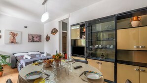 Un área de comedor con una mesa lista para dos personas, un sofá y un televisor al fondo.